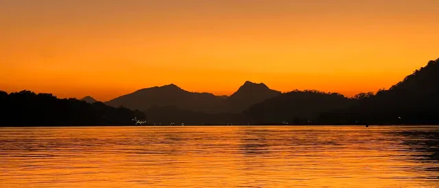 Hills silhouetted against an orange sunset over a river.